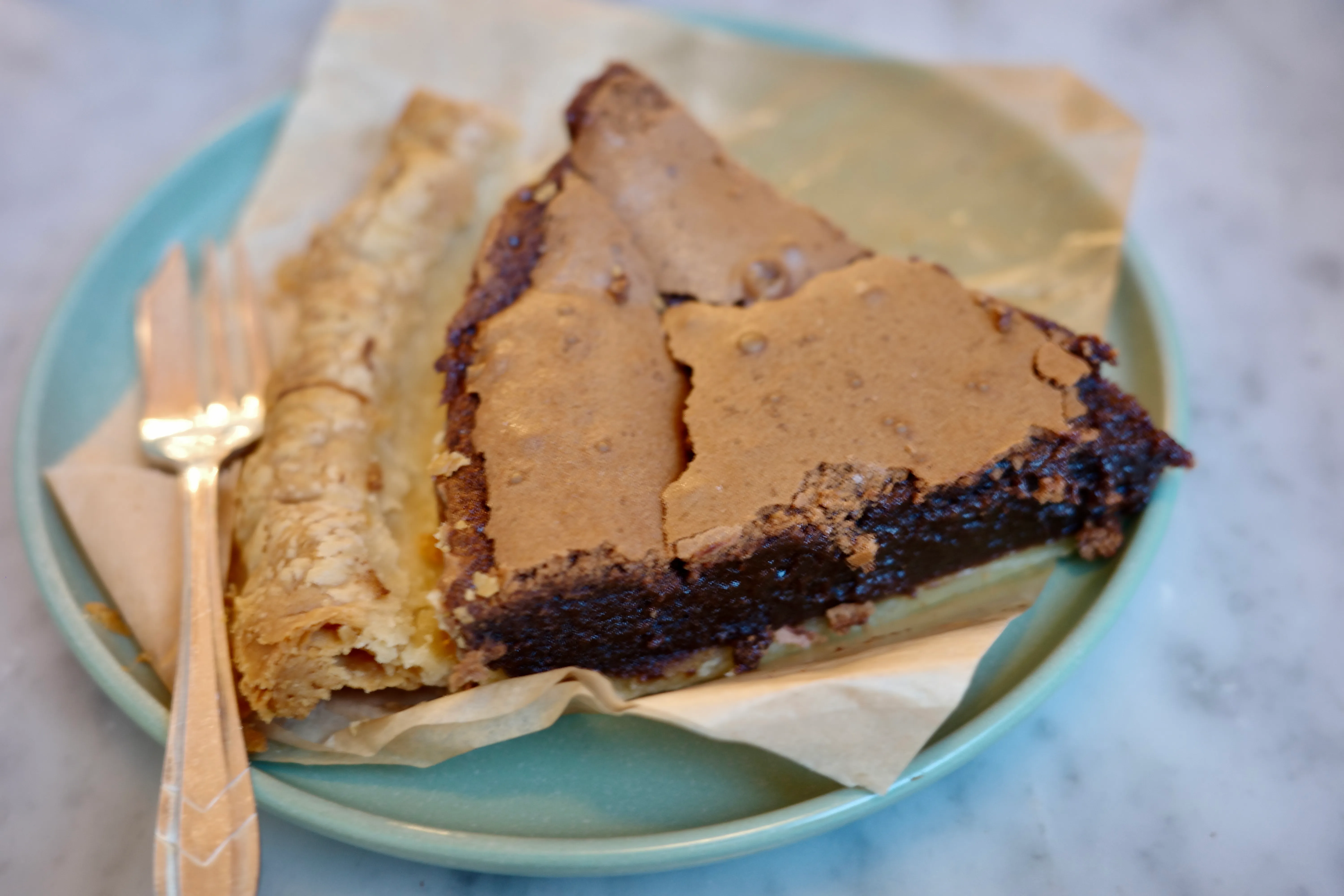 A slice of salty chocolate chess pie on a teal plate, crackly meringue-like top over dark fudgy filling, gold fork to the side