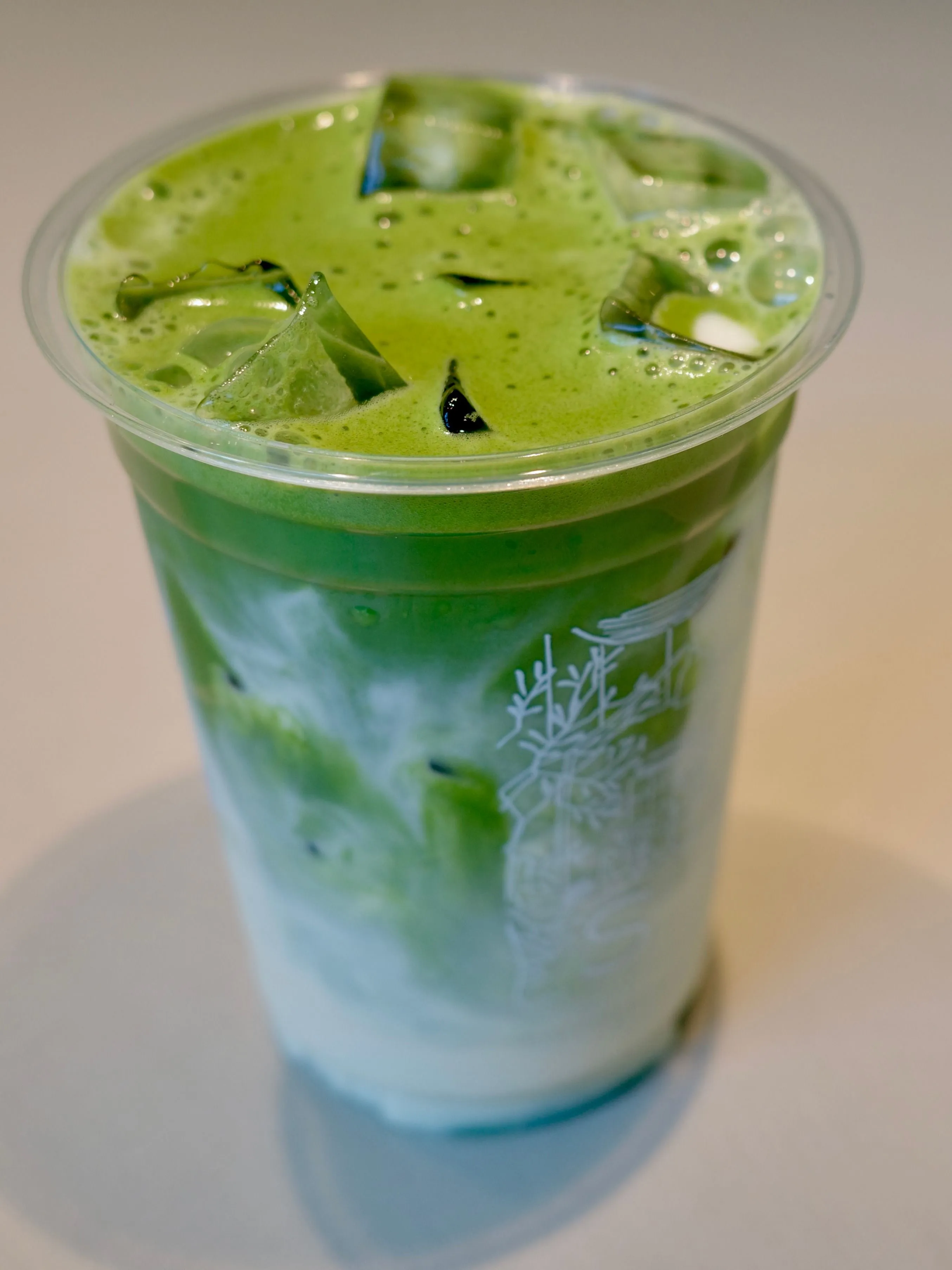 Iced matcha latte with oat milk in a plastic cup, vivid green over white