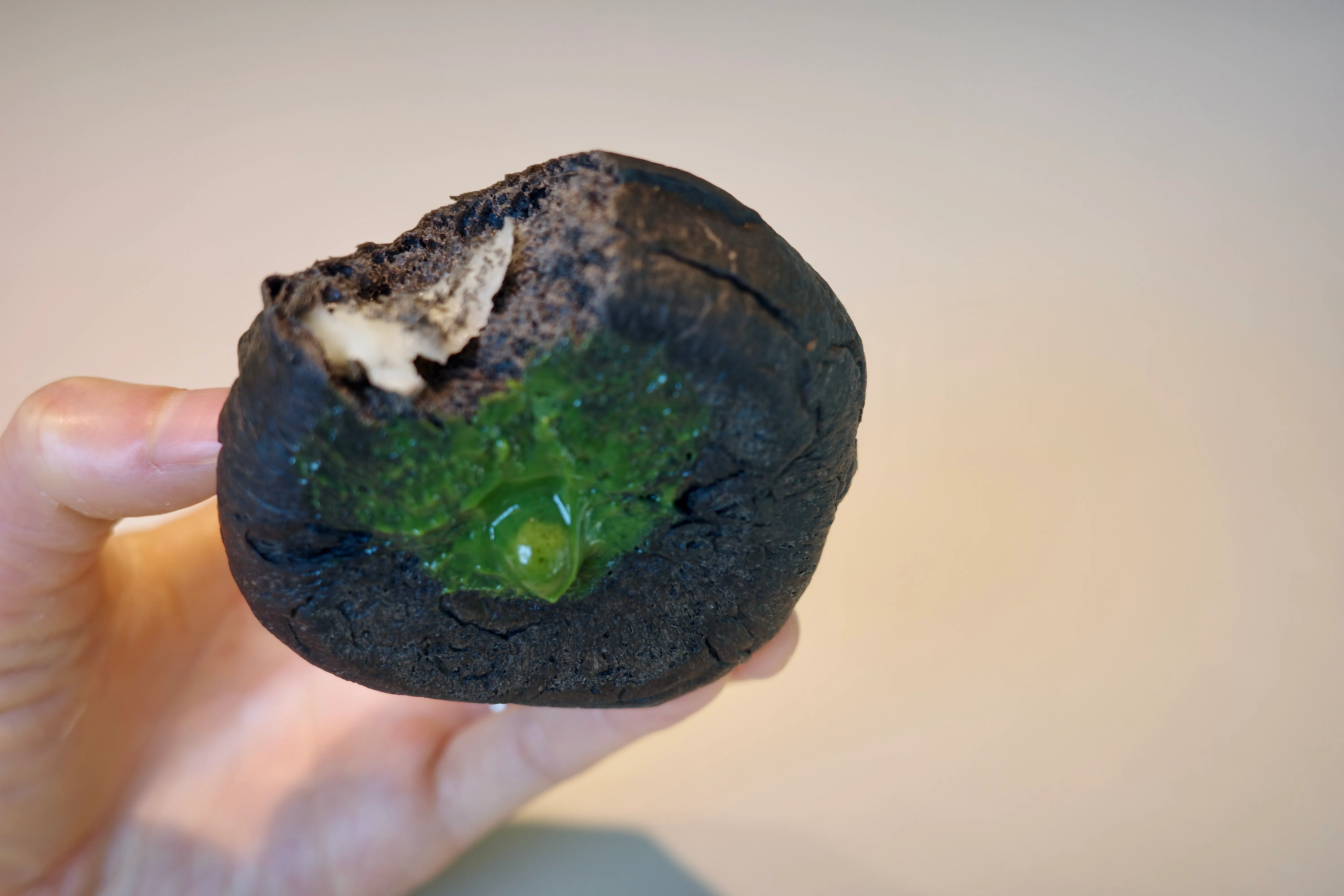 A bitten charcoal-black mochi bun with vivid green matcha paste oozing out